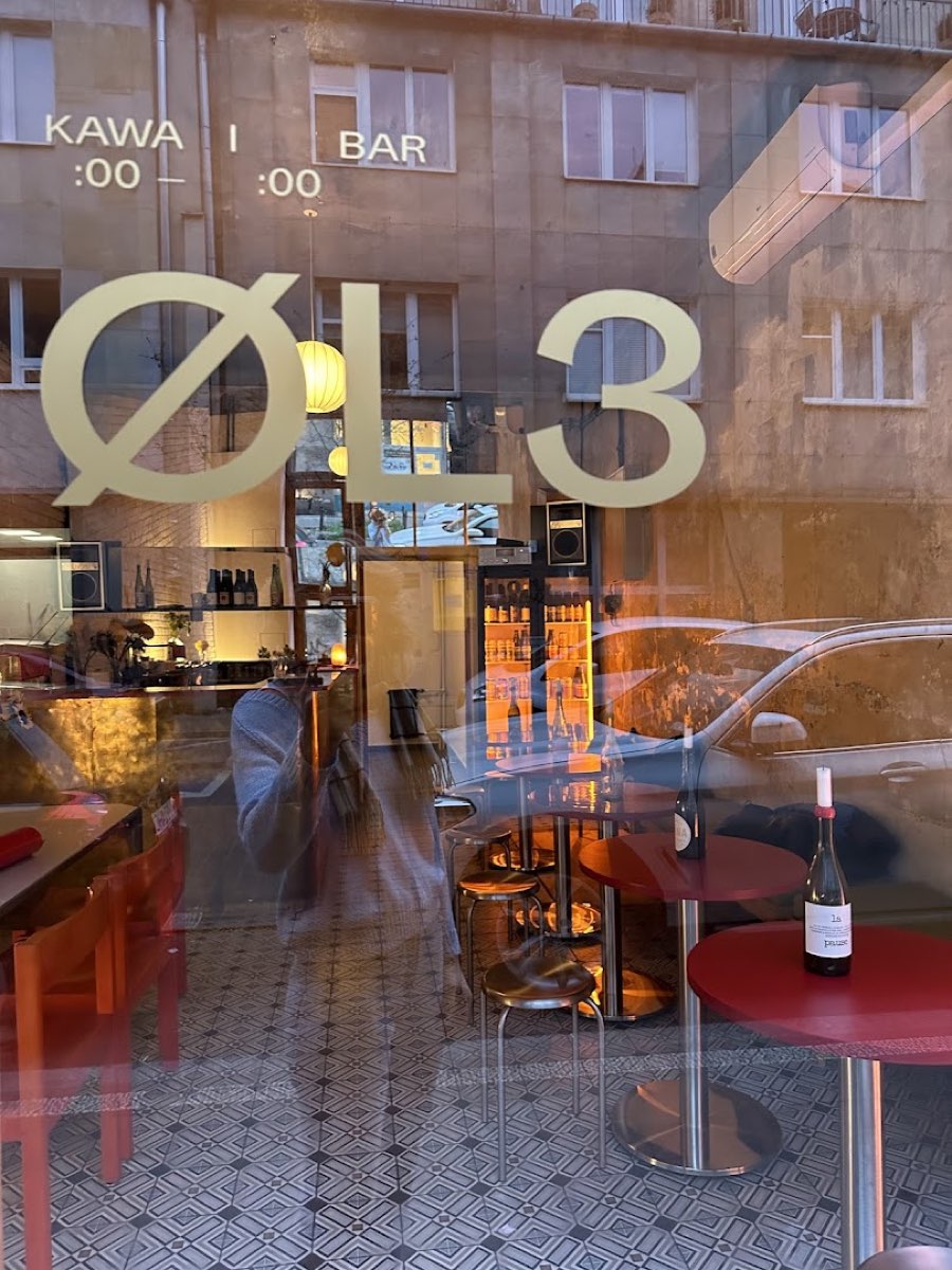 Złote logo ØL3 na witrynie z napisem KAWA I BAR i czerwone stoliki w środku