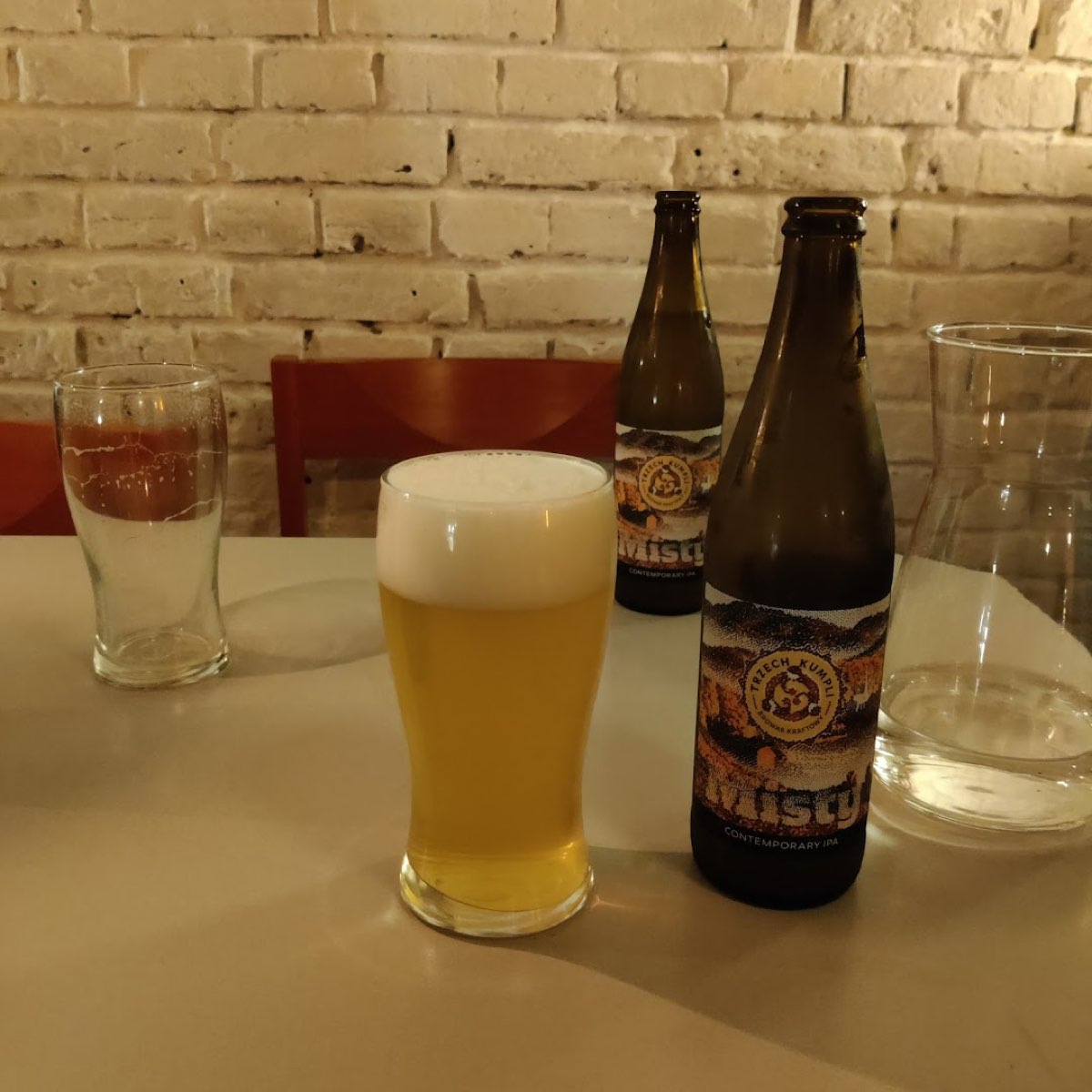 Kufel jasnego piwa i butelki współczesnego IPA na tle białej cegły